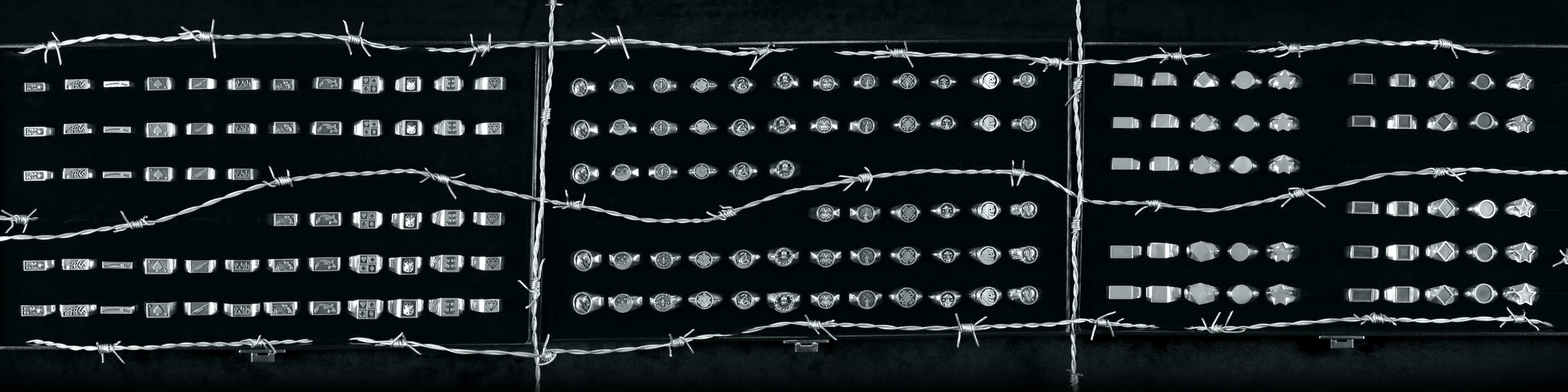 Rows of completed Jack Sterling sterling silver signet rings displayed in cases behind barbed wire, brand collection banner